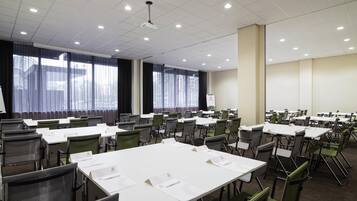 A conference room with multiple tables and chairs, large windows with curtains, and a whiteboard.