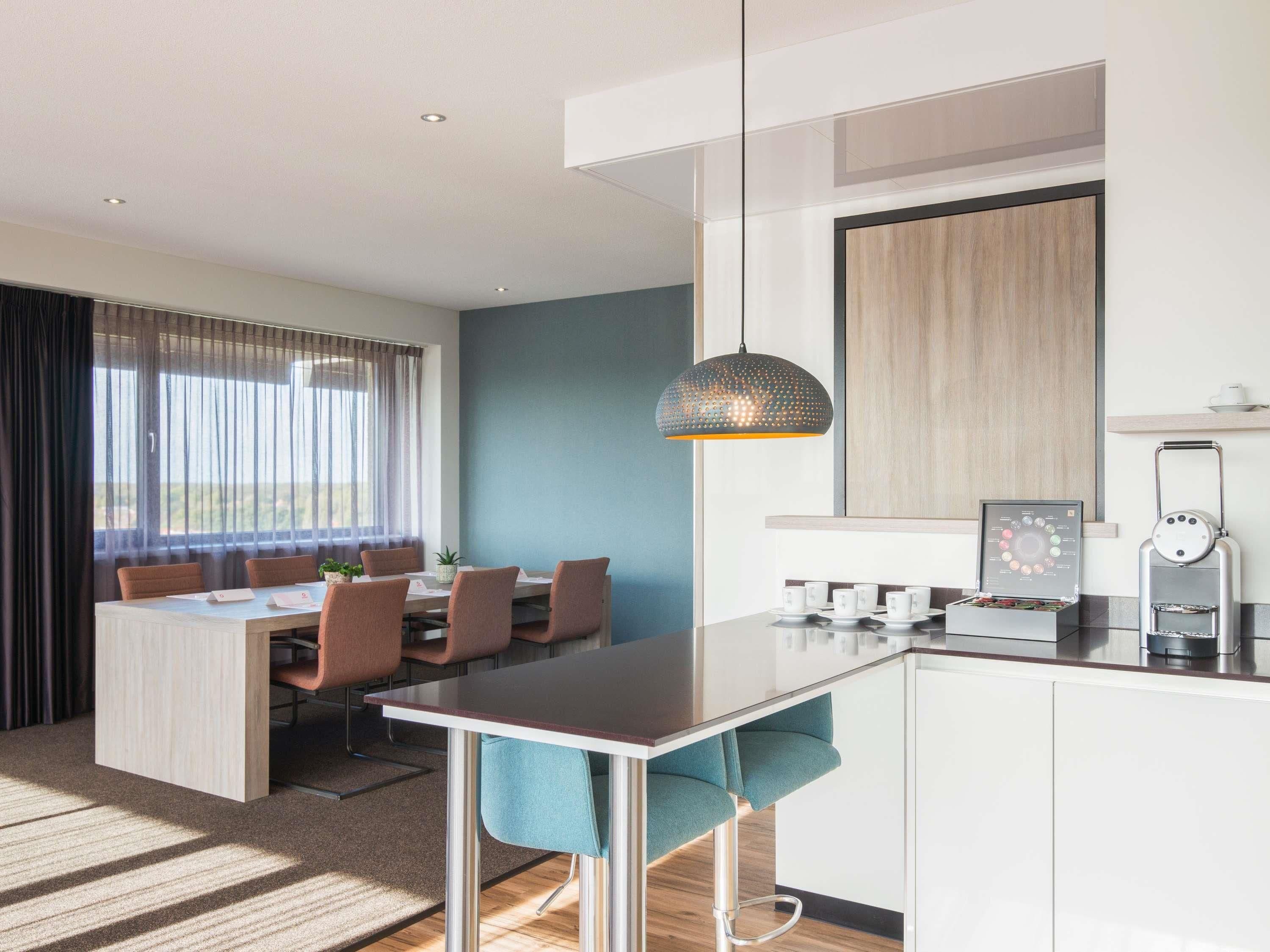 A modern kitchen with a dining area, a coffee machine, and a view of the outdoors.
