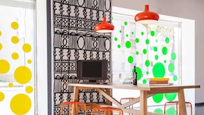 A modern interior with a wooden desk, orange chairs, a black monitor, and red pendant lights. - ibis Styles Brindisi (Brindisi)