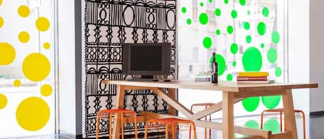 A modern interior with a wooden desk, orange chairs, a black monitor, and red pendant lights.