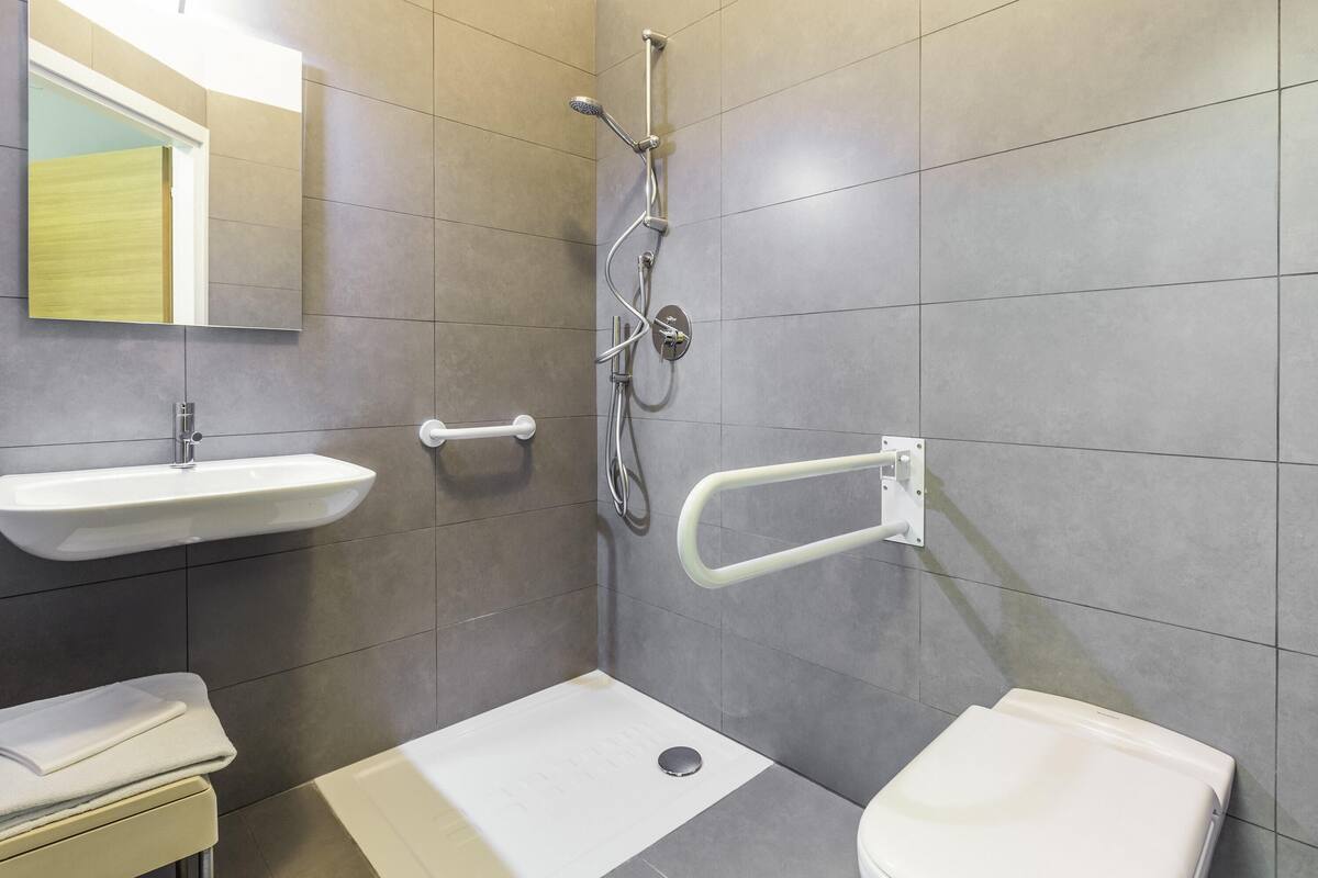 Een moderne badkamer met douche, wastafel, toilet en handgrepen.