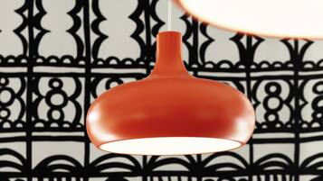 Uma luminária pendente com cúpula vermelha suspensa diante de um papel de parede estampado.