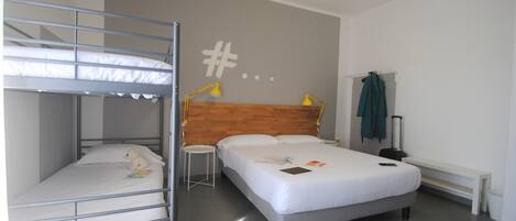 Una habitación con una cama litera, una cama individual, un escritorio, una silla, una lámpara y una maleta.