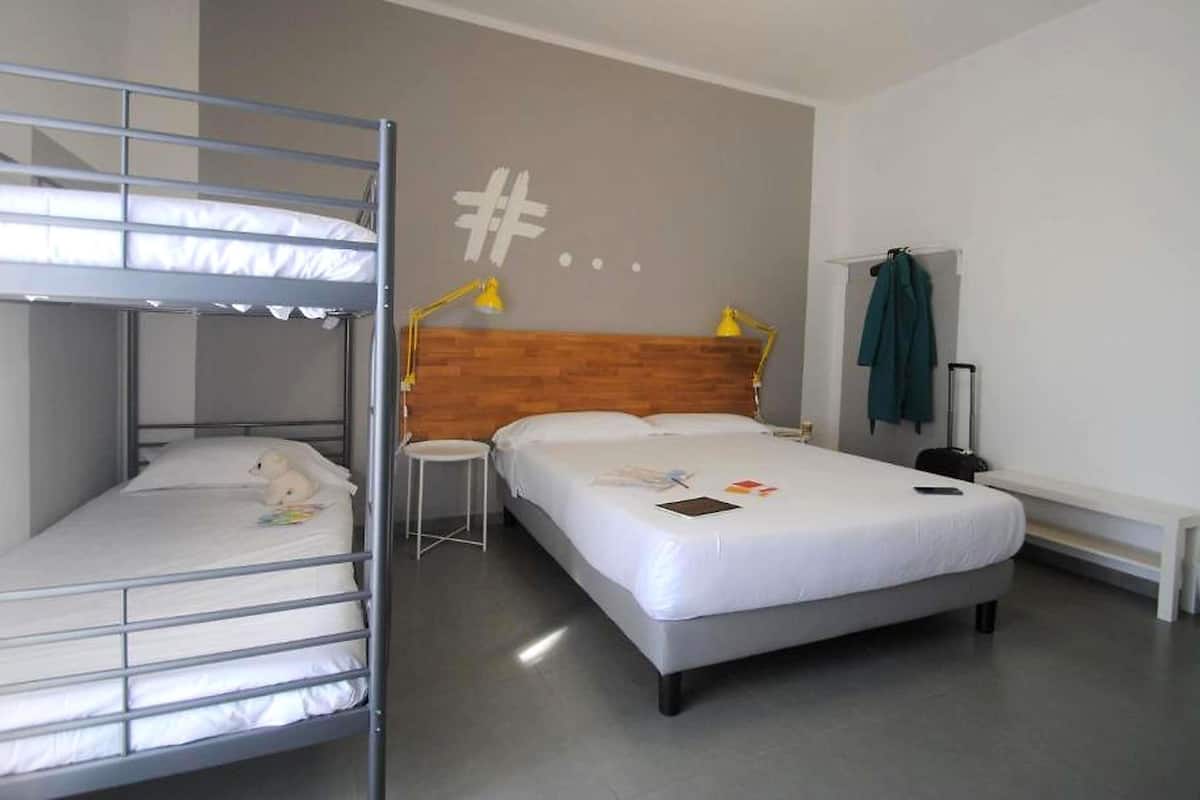 Una habitación con literas, una cama individual, un cabecero de madera, un escritorio, una silla y una maleta.