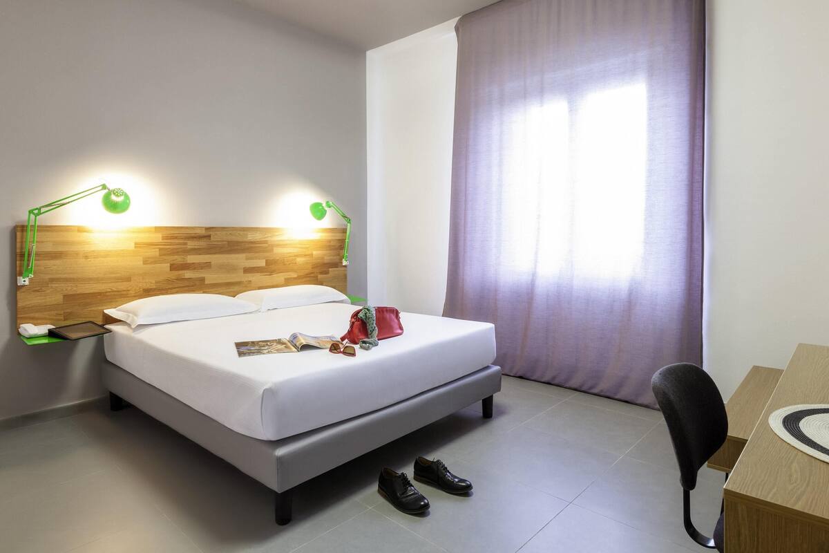 Een hotelkamer met een bed, bedlampjes, een bureau en een stoel.