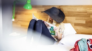 A person lying on a bed with a wooden headboard, reading a book under a green desk lamp. - ibis Styles Brindisi (Brindisi)