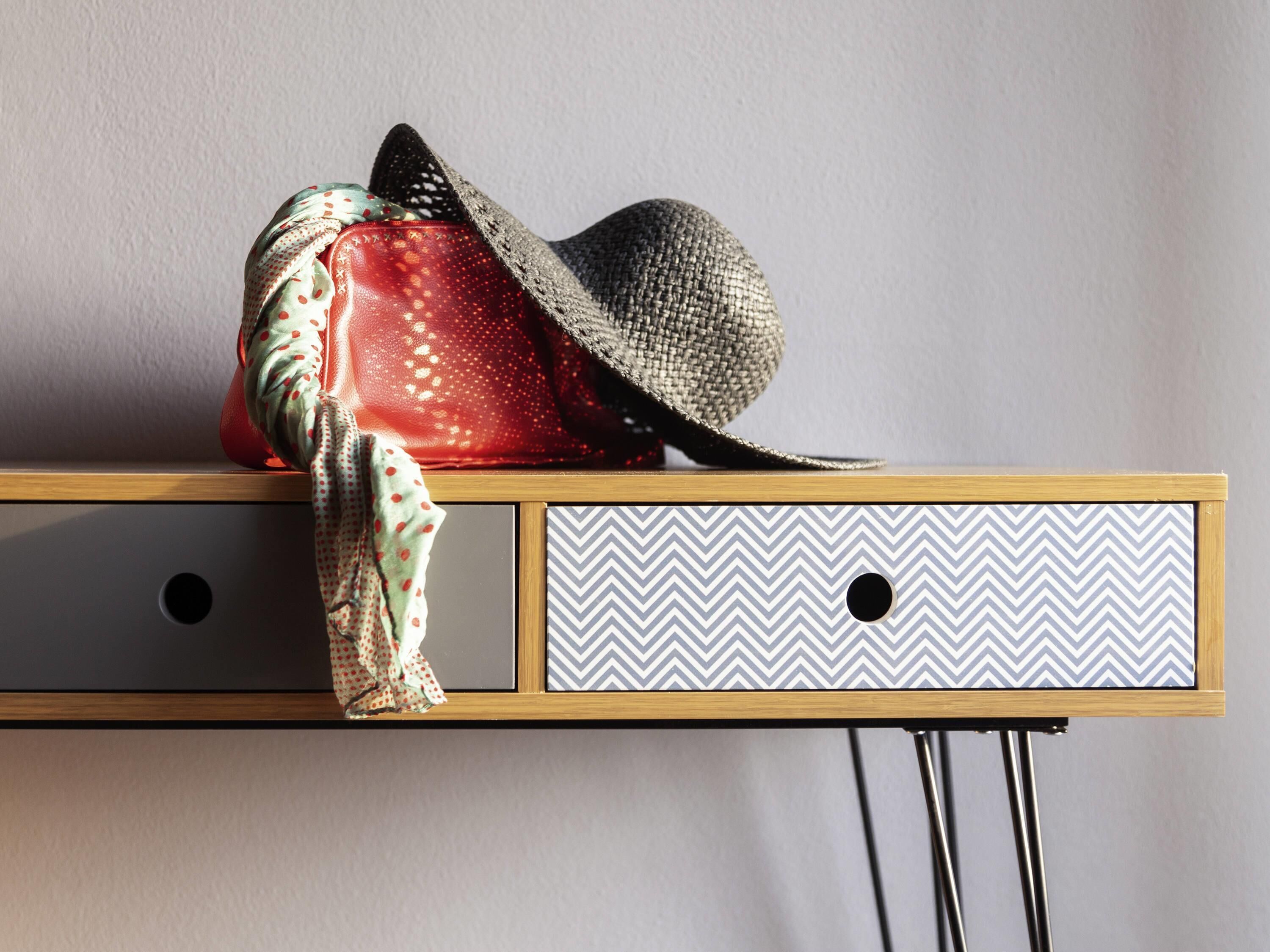 A wooden console table with a patterned drawer, a red polka-dotted bag, and a gray hat.