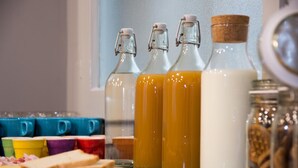 Eine Küchenarbeitsplatte mit Glasflaschen, die verschiedene Flüssigkeiten enthalten, bunten Tassen sowie Käse- und Brotscheiben.