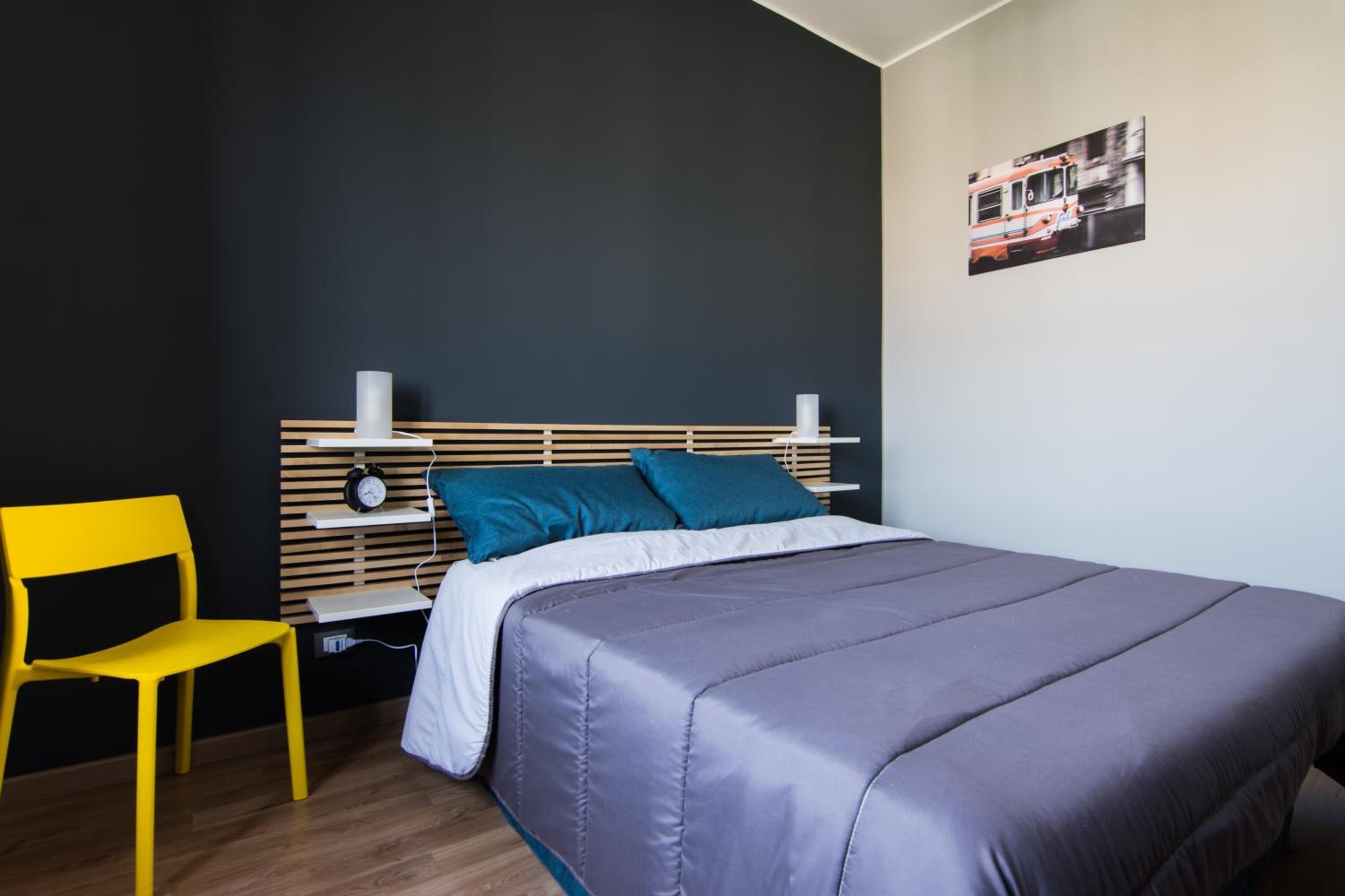 Une chambre à coucher comprenant un lit, une chaise, une table de chevet et une horloge fixée au mur.