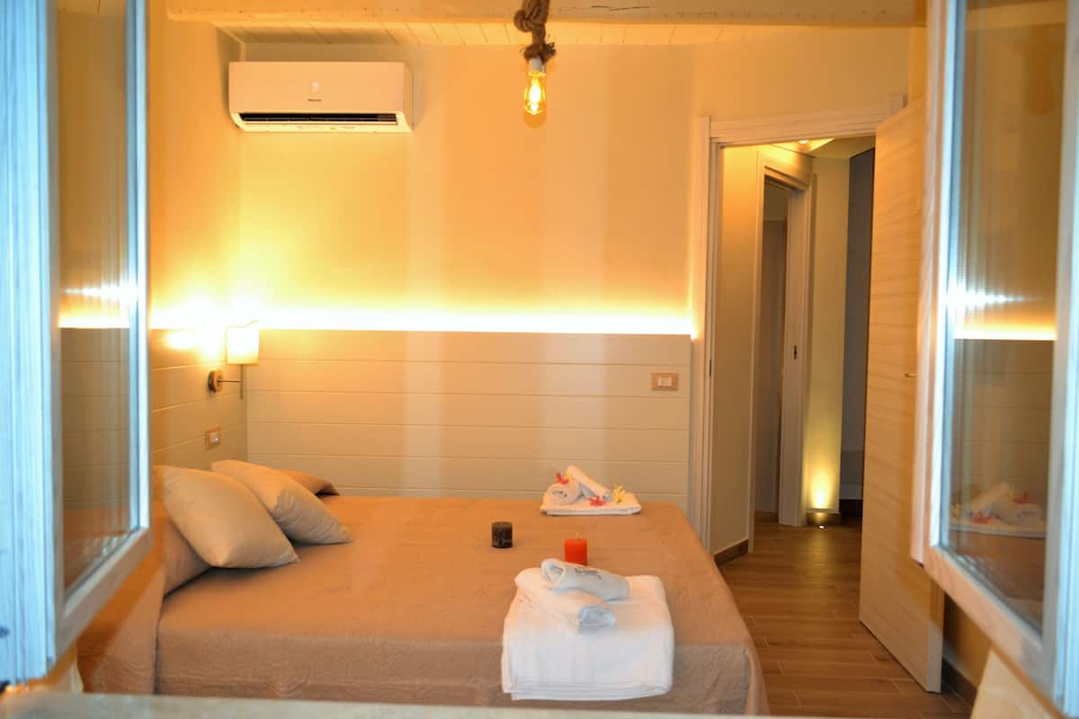 Quarto de hotel com uma cama, mesa de cabeceira, luminária e ar condicionado.