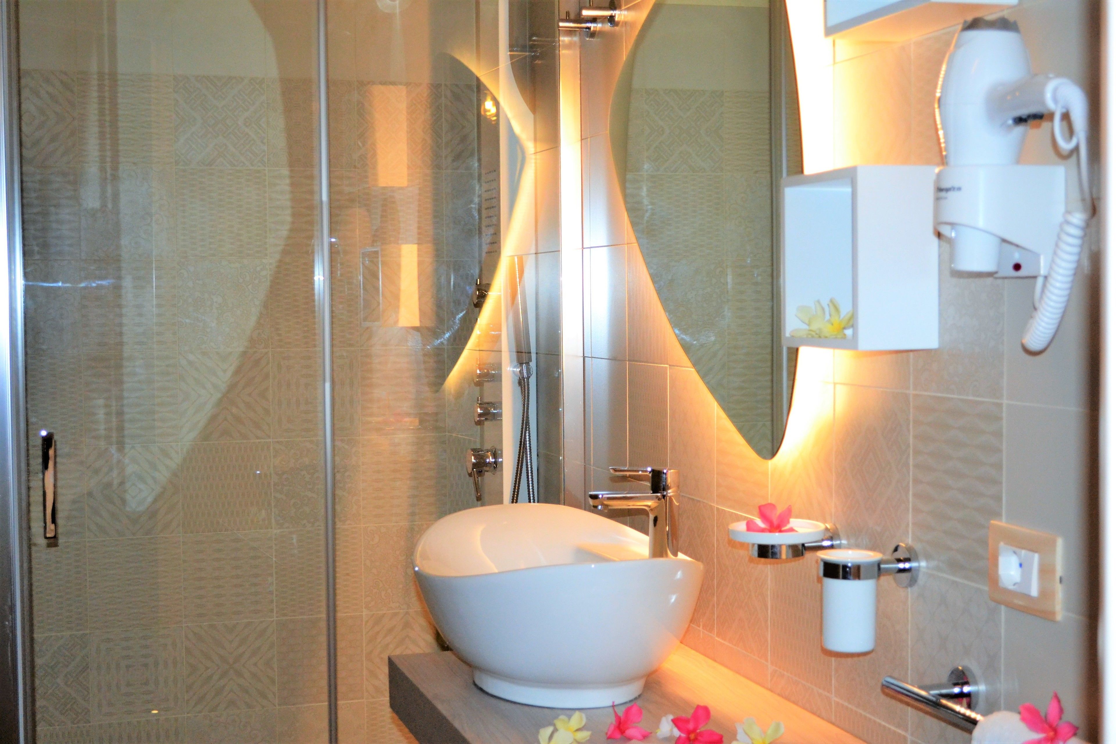 A modern bathroom with a glass shower enclosure, a freestanding white sink, and a hairdryer mounted on the wall.