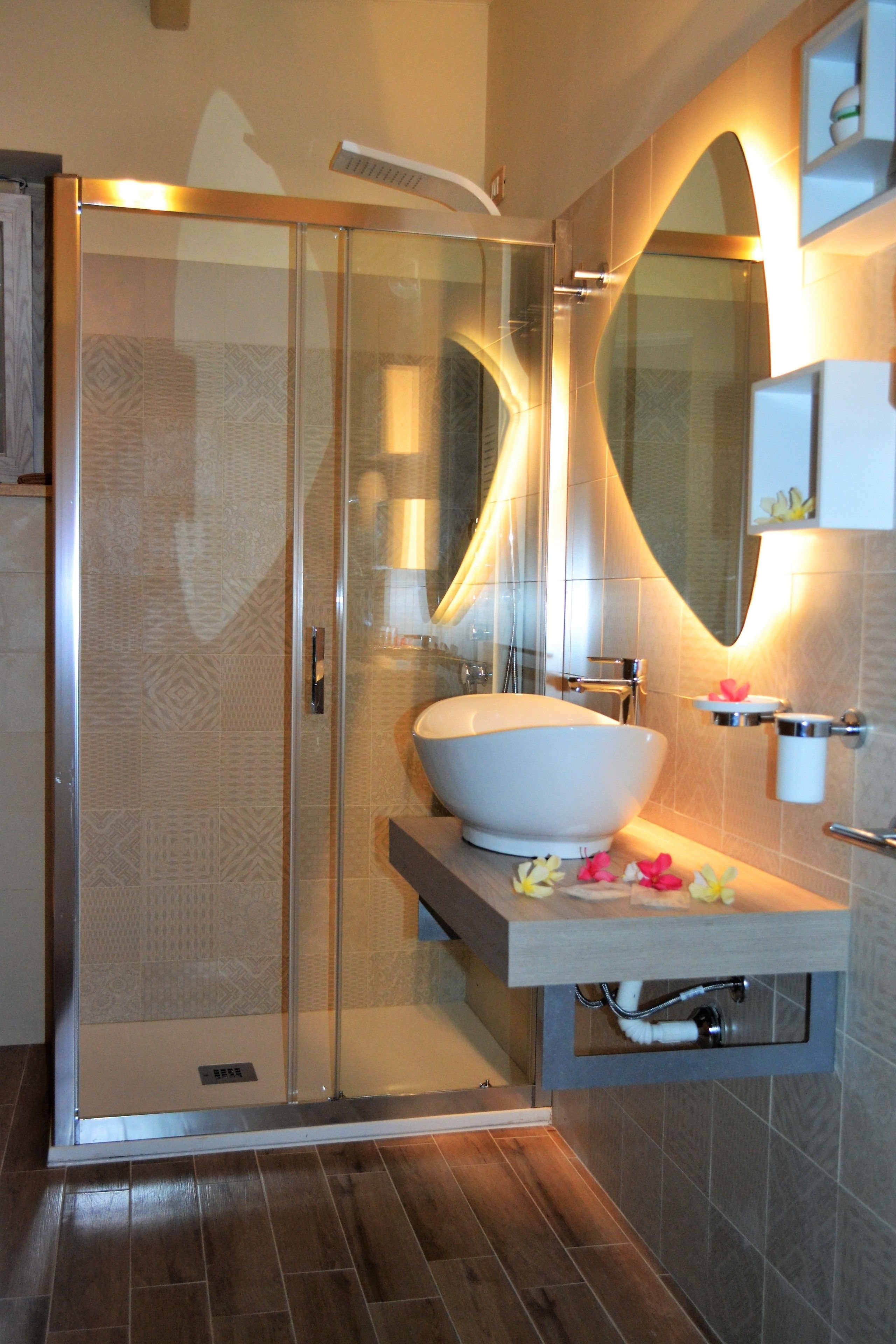 Ein modernes Badezimmer mit einer begehbaren Glasdusche, einem großen weißen Waschbecken und einem Spiegel mit integrierter Beleuchtung.
