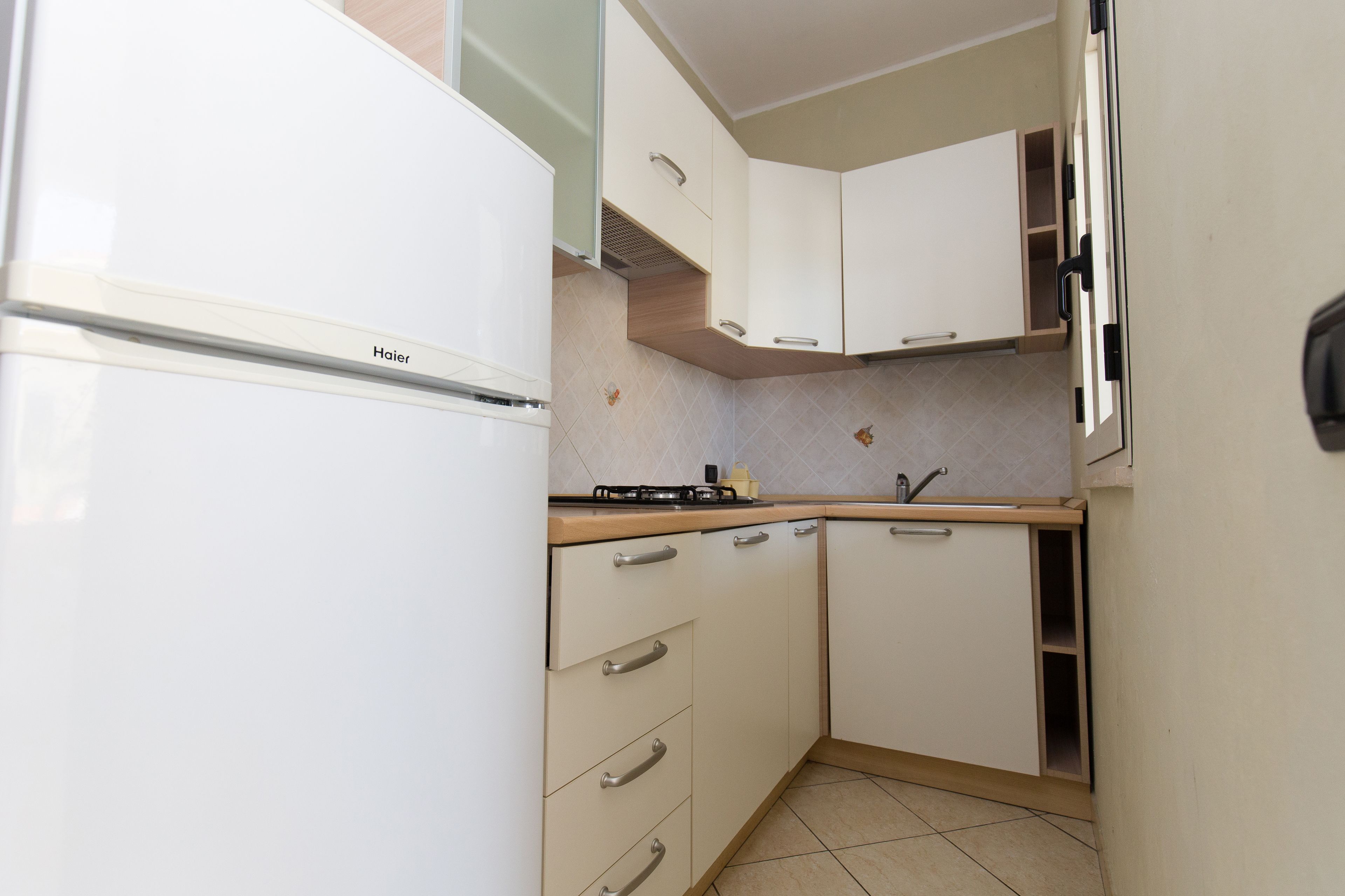A compact kitchen with white cabinets, a Haier refrigerator, and a small countertop.