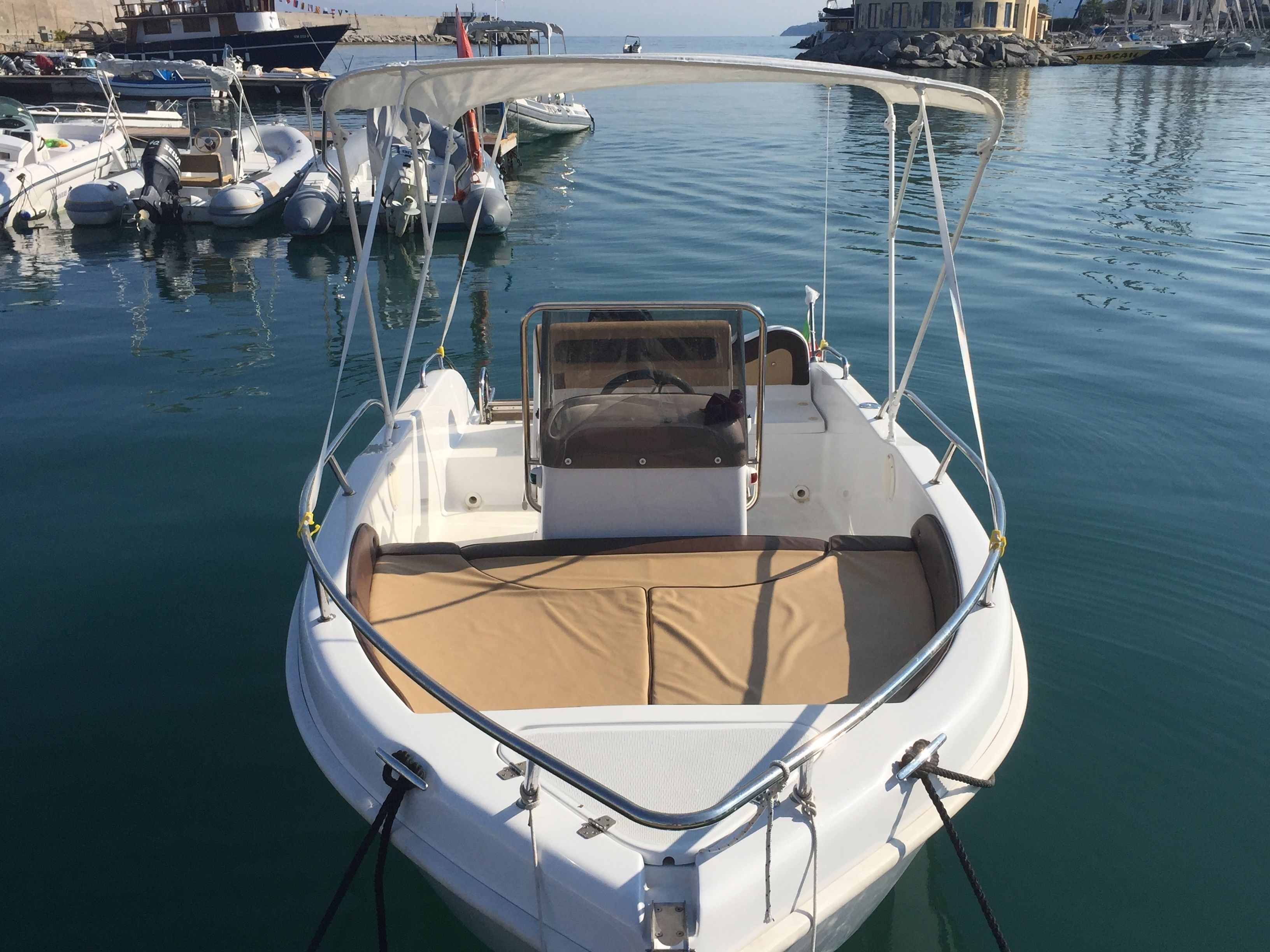 Un pequeño barco motorizado amarrado en un puerto deportivo con una zona de estar cubierta y una cabina.