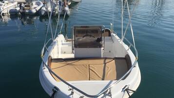 Un pequeño barco motorizado amarrado en un puerto deportivo con una zona de estar cubierta y una cabina.
