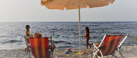 A beach scene with two striped beach chairs and a striped umbrella.