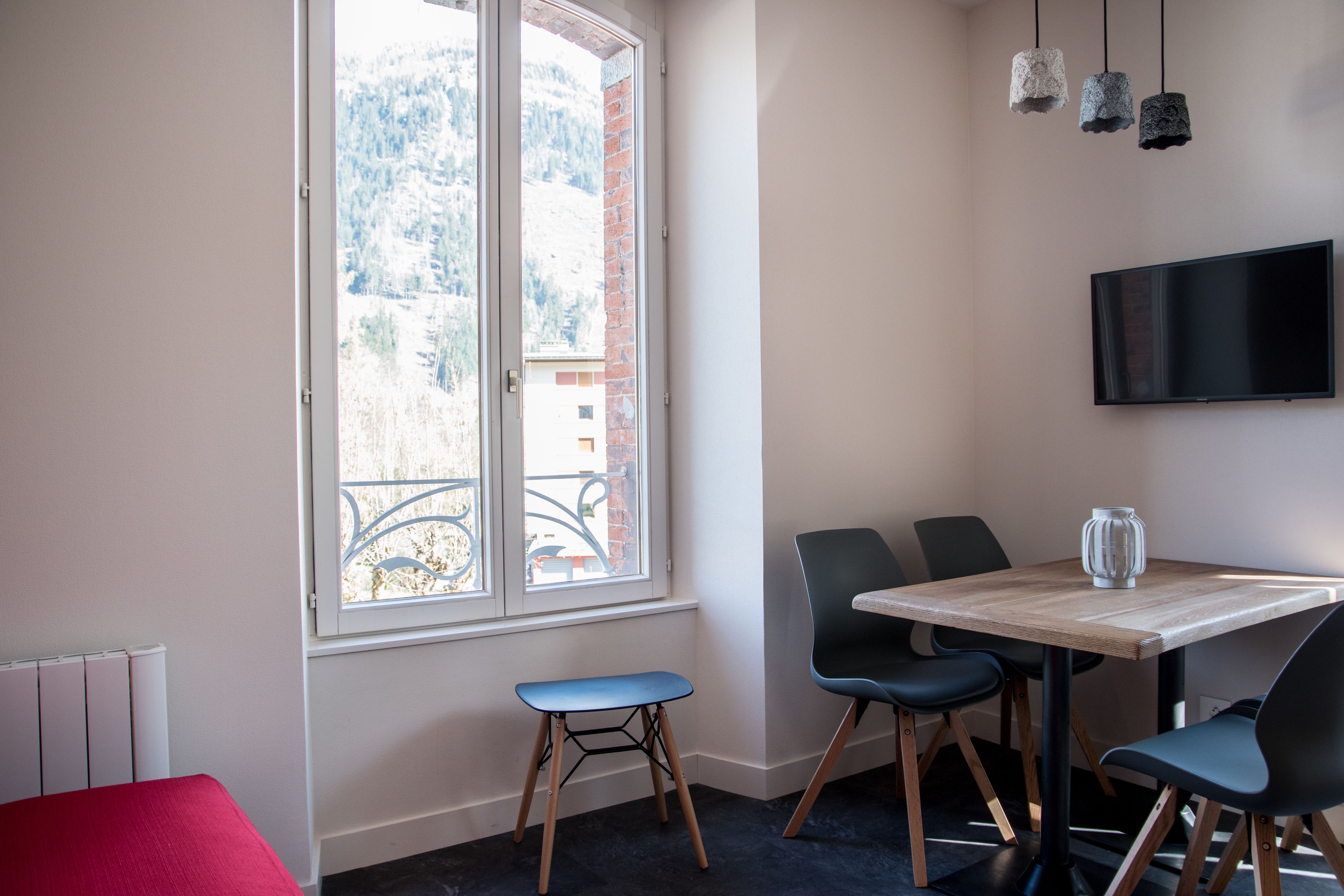 Un comedor moderno con una mesa, sillas, un taburete pequeño y un televisor montado en la pared.