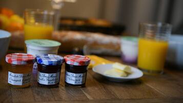 A breakfast table with jars of jam, a plate of butter, and glasses of orange juice.