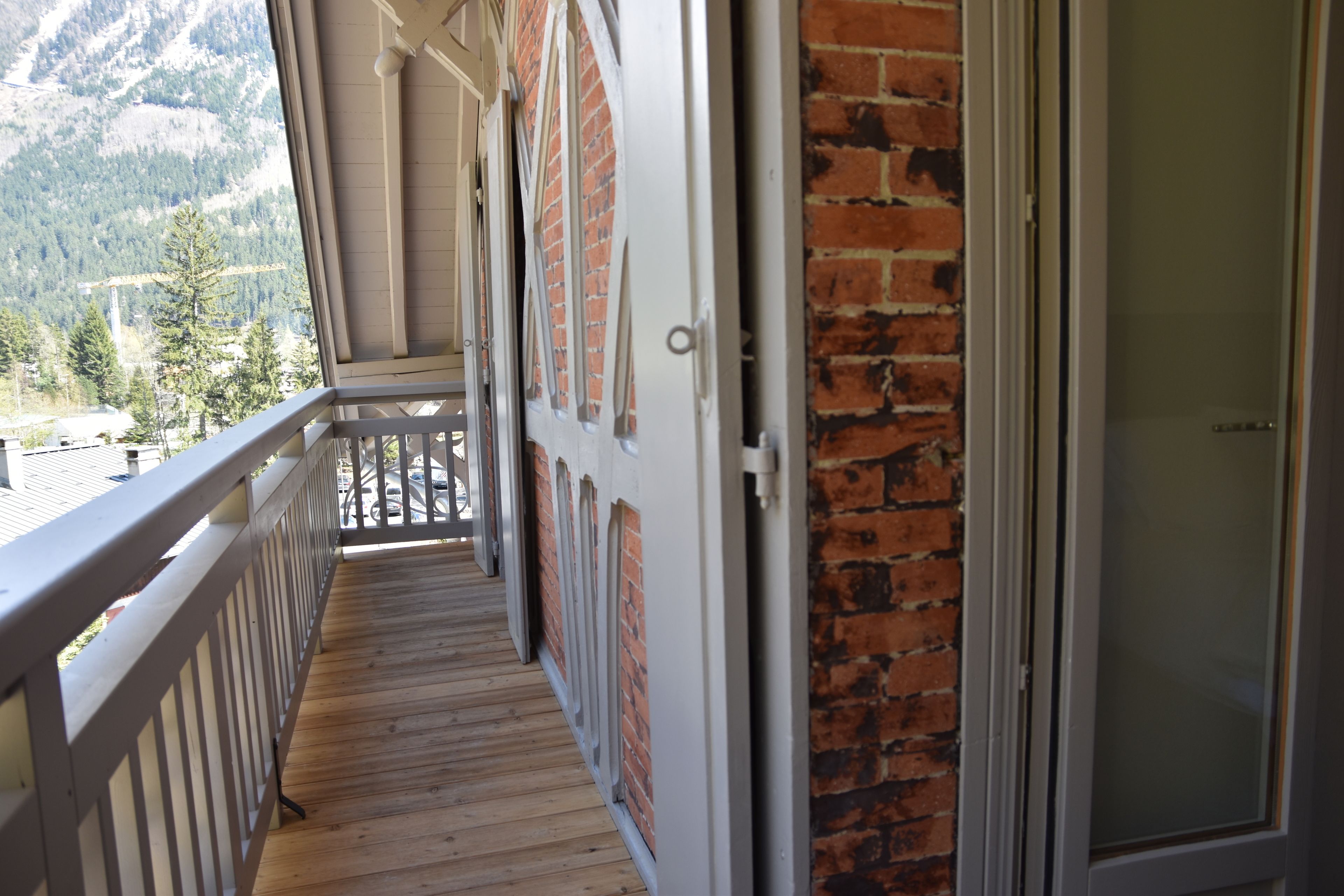 A wooden balcony with a metal railing, a brick wall, and a door.