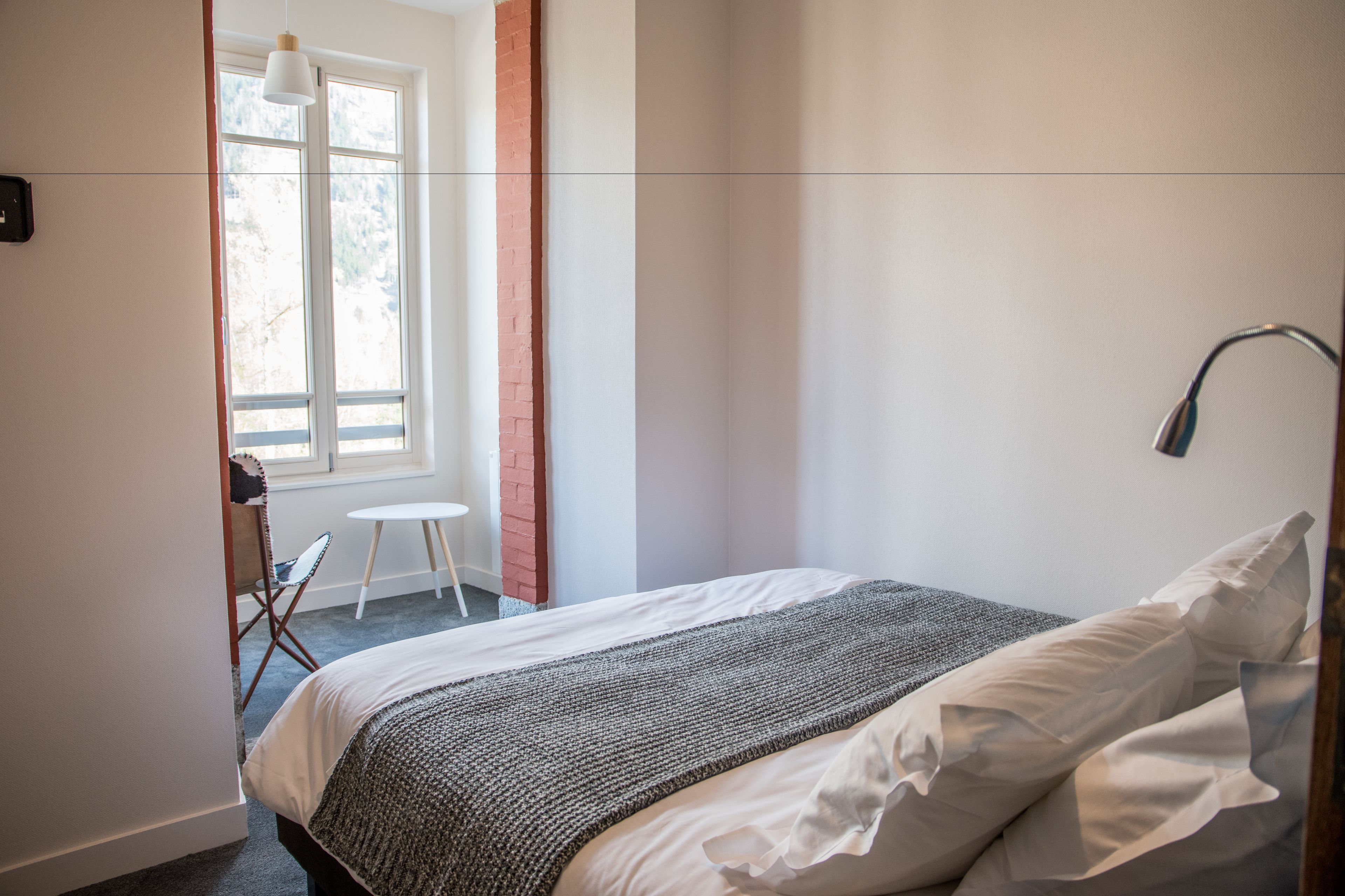 Une chambre à coucher avec un lit, une chaise, une petite table et une fenêtre.