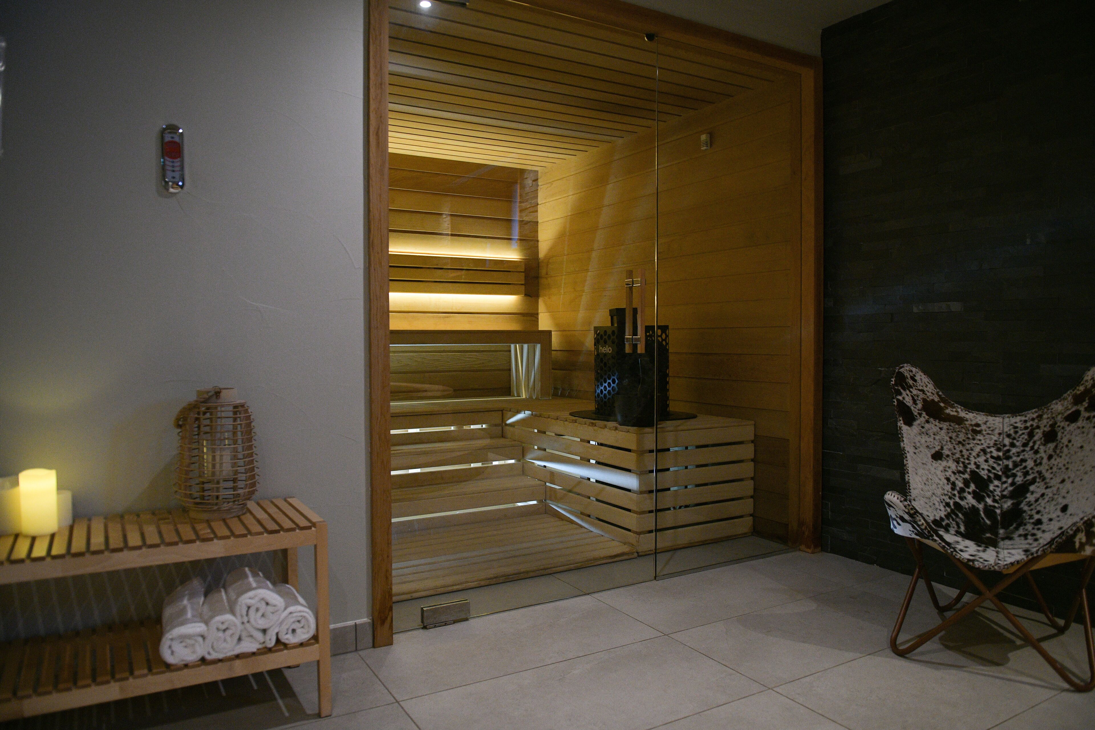 A spa room with wooden benches, a glass sauna door, and a chair.