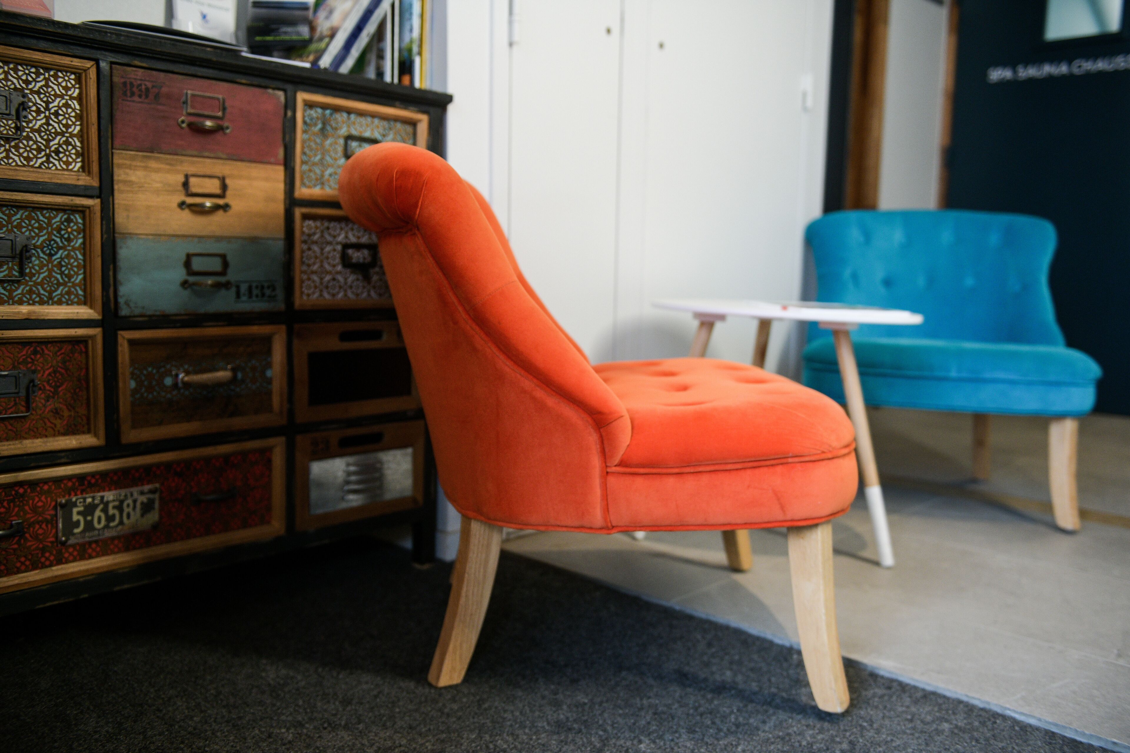 A room with a vintage-style chest of drawers, a modern orange chair, and a small white table.