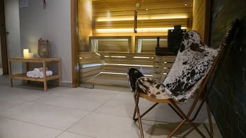 Una stanza spa con una panca in legno, una sedia con cuscino maculato e un tavolino con asciugamani e una candela.