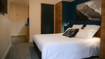 Une chambre à coucher comprenant un lit, une table de chevet, une lampe fixée au mur et un grand tableau encadré représentant une montagne.