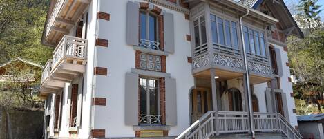 A two-story building with a balcony, a staircase, and a stone foundation.