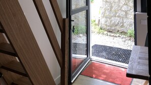 Una escalera conduce a una habitación con un amplio ventanal, un muro de piedra en el exterior y un felpudo rojo en la entrada.