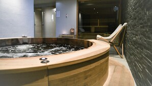 Una bañera de hidromasaje de madera con una silla de madera cerca, un banco de madera y una pared de ladrillo.