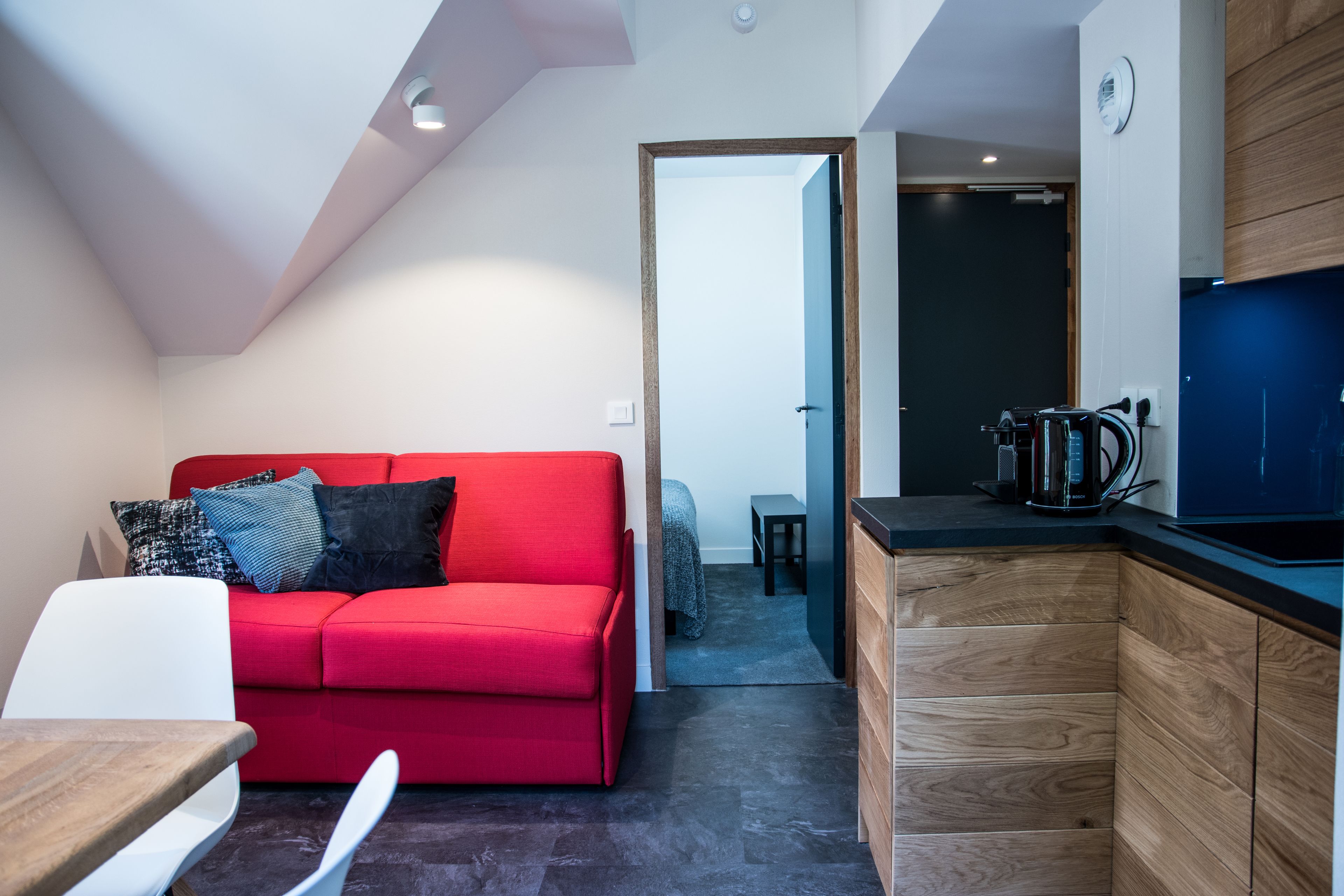 A modern living space with a red sofa, a wooden cabinet, and a kitchen area.