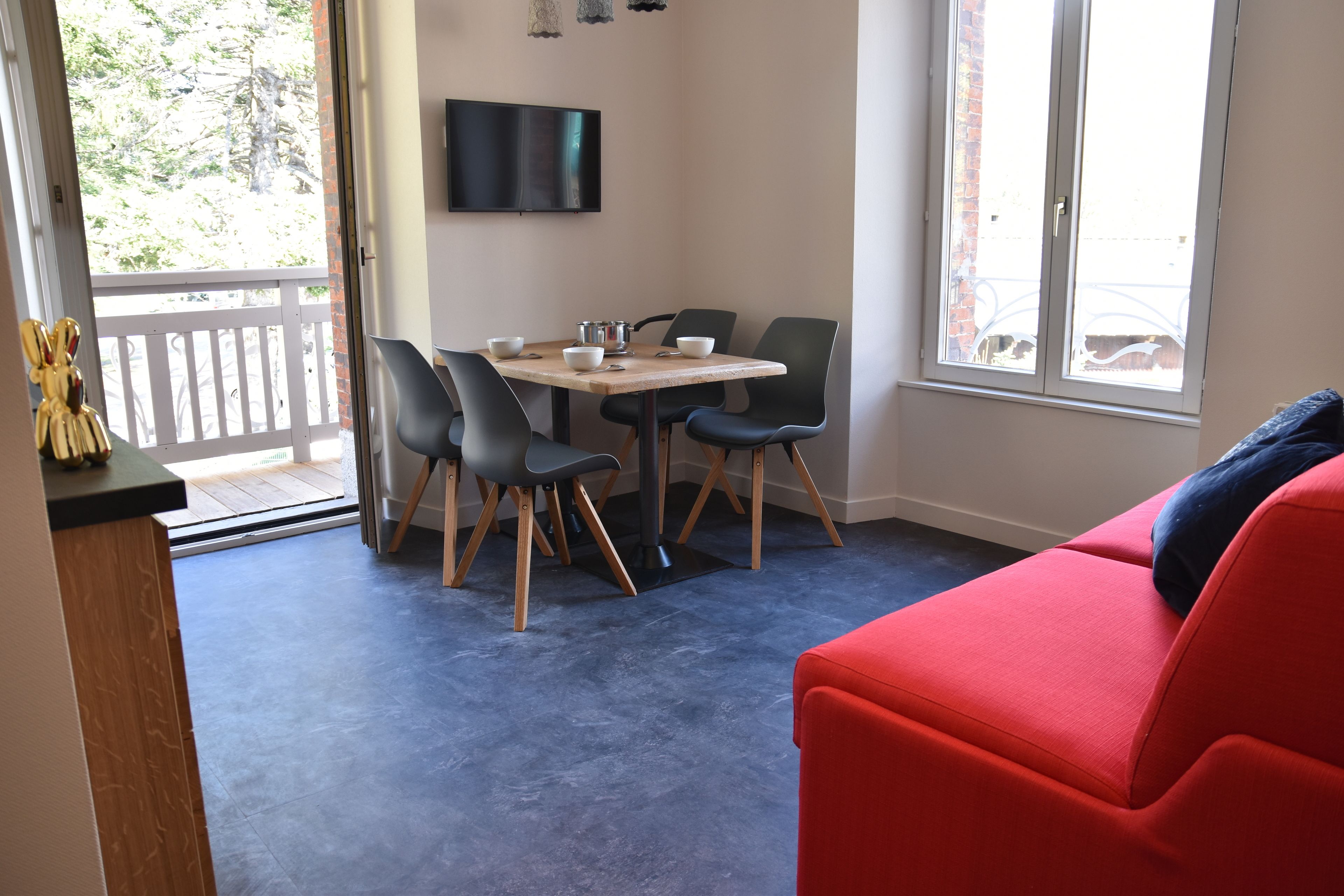 Ein Essbereich mit Tisch und Stühlen, einem Fernseher an der Wand und einem roten Sofa im Vordergrund.