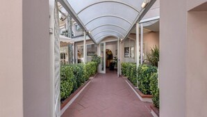A covered corridor with a tiled floor, flanked by neatly trimmed hedges and glass railings. - Hotel Azzurra (Pietrasanta)
