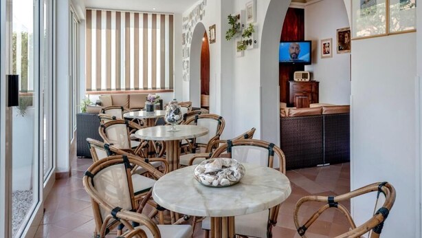 A dining area with wicker chairs and round tables, a television, and framed pictures on the walls. - Hotel Azzurra (Pietrasanta)