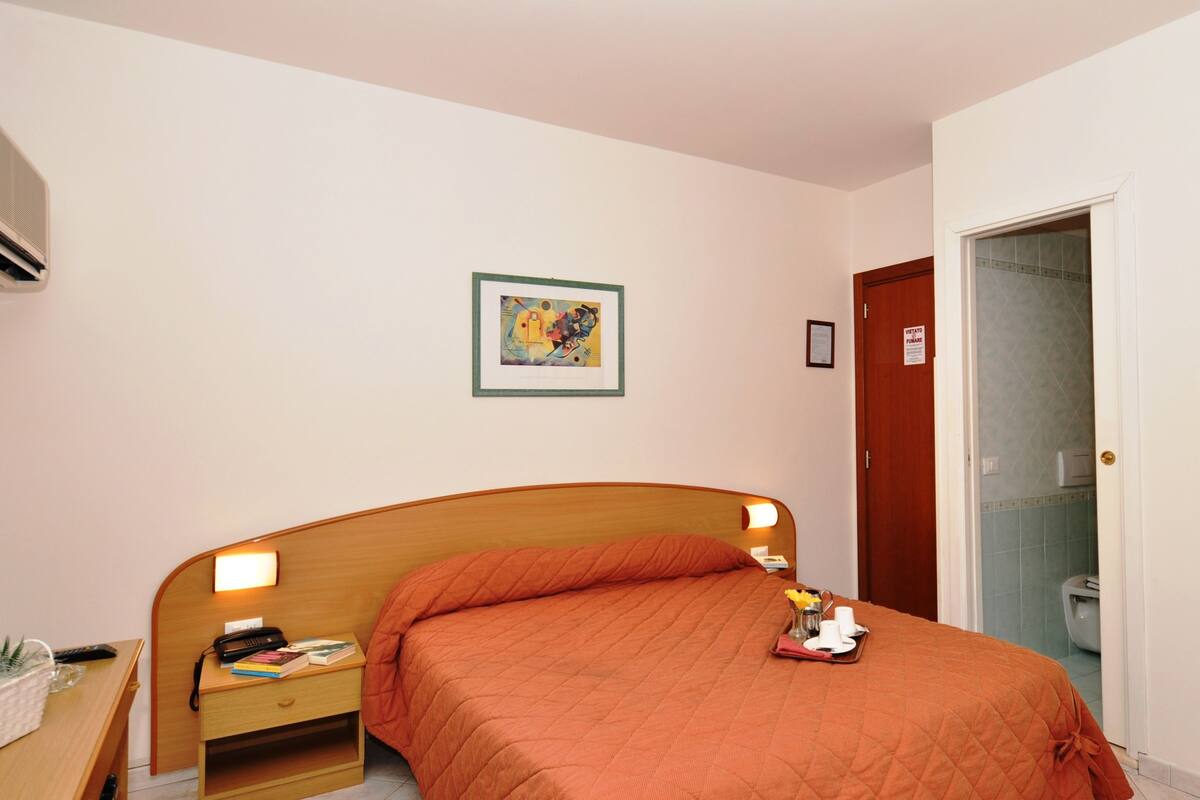 Habitación de hotel con cama de madera, lámparas de noche, un cuadro enmarcado en la pared y una puerta con un letrero de 'No Entrar'.