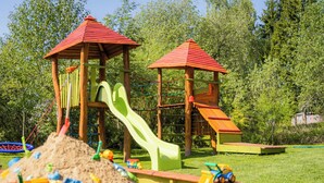 A playground with two play structures, including slides and climbing areas, surrounded by green grass and trees. - Apartmány Nad Rybníky (Horni Plana)