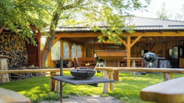An outdoor dining area with a grill, a table with a bowl, and a stone fire pit. - Apartmány Nad Rybníky (Horni Plana)