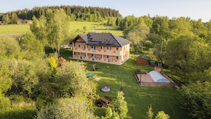 A two-story building with a sloped roof, surrounded by a well-maintained lawn and trees. - Apartmány Nad Rybníky (Horni Plana)