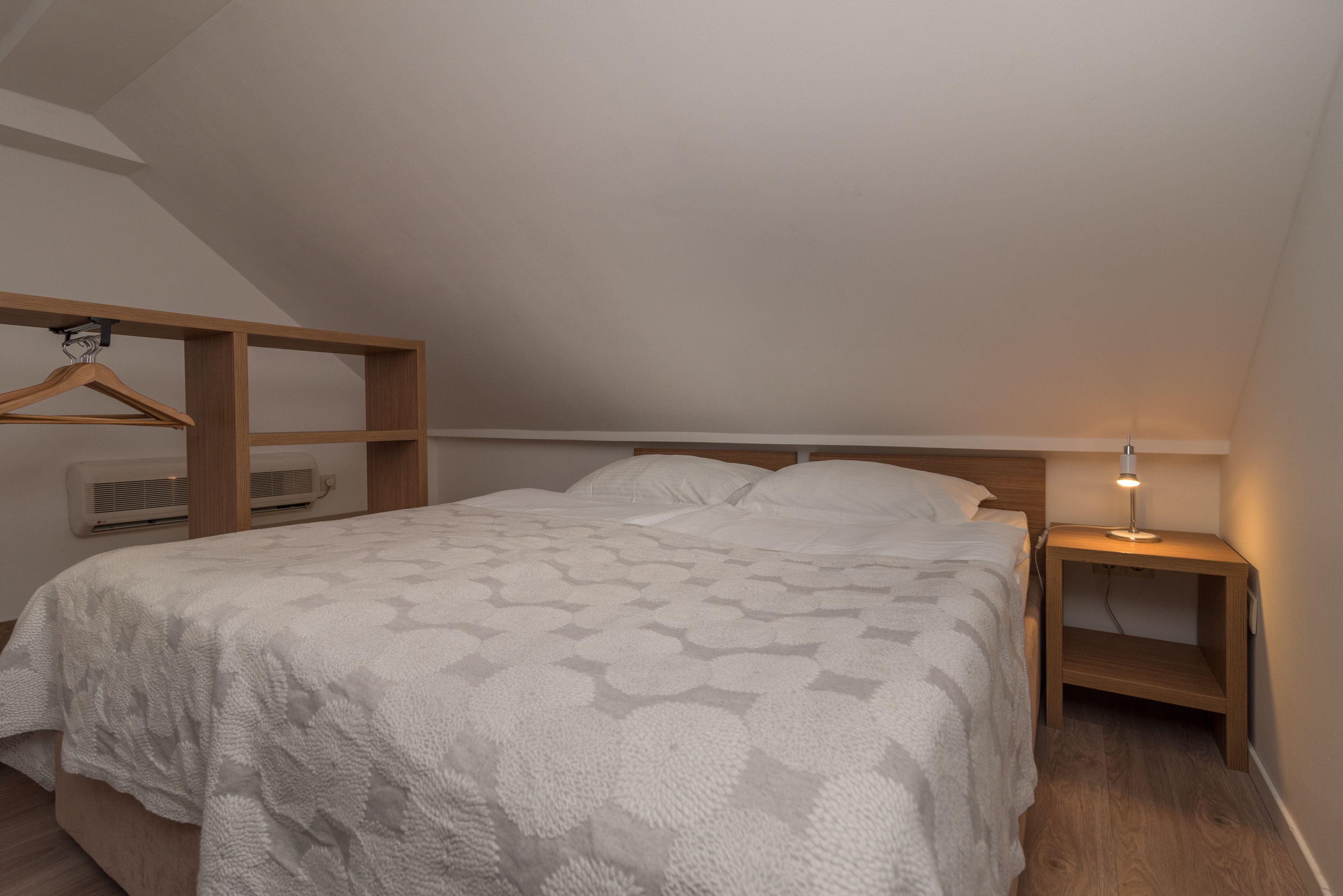 Un dormitorio con cama, mesita de noche de madera con lámpara, armario de madera y equipo de aire acondicionado.