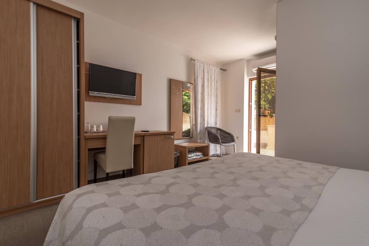 A hotel room with a bed, a desk, a chair, a television, and a sliding door to a balcony.
