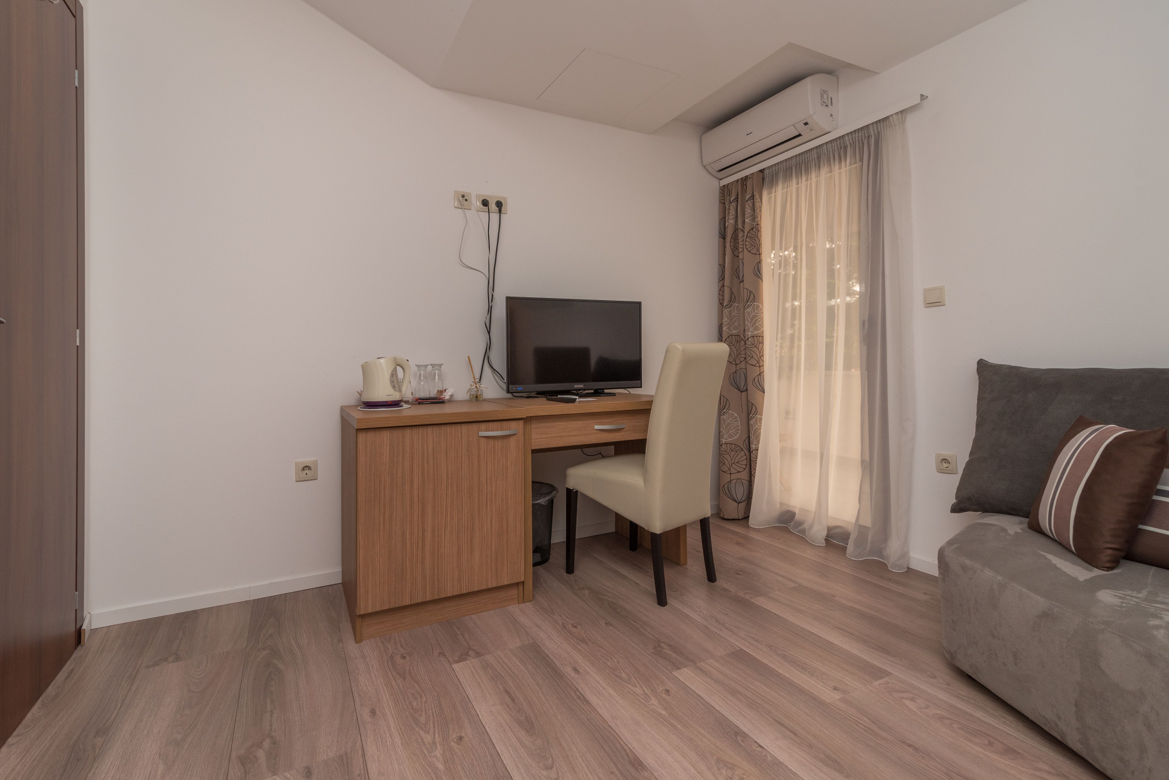 A small, modern room with a wooden desk, a chair, a television, and a sofa.