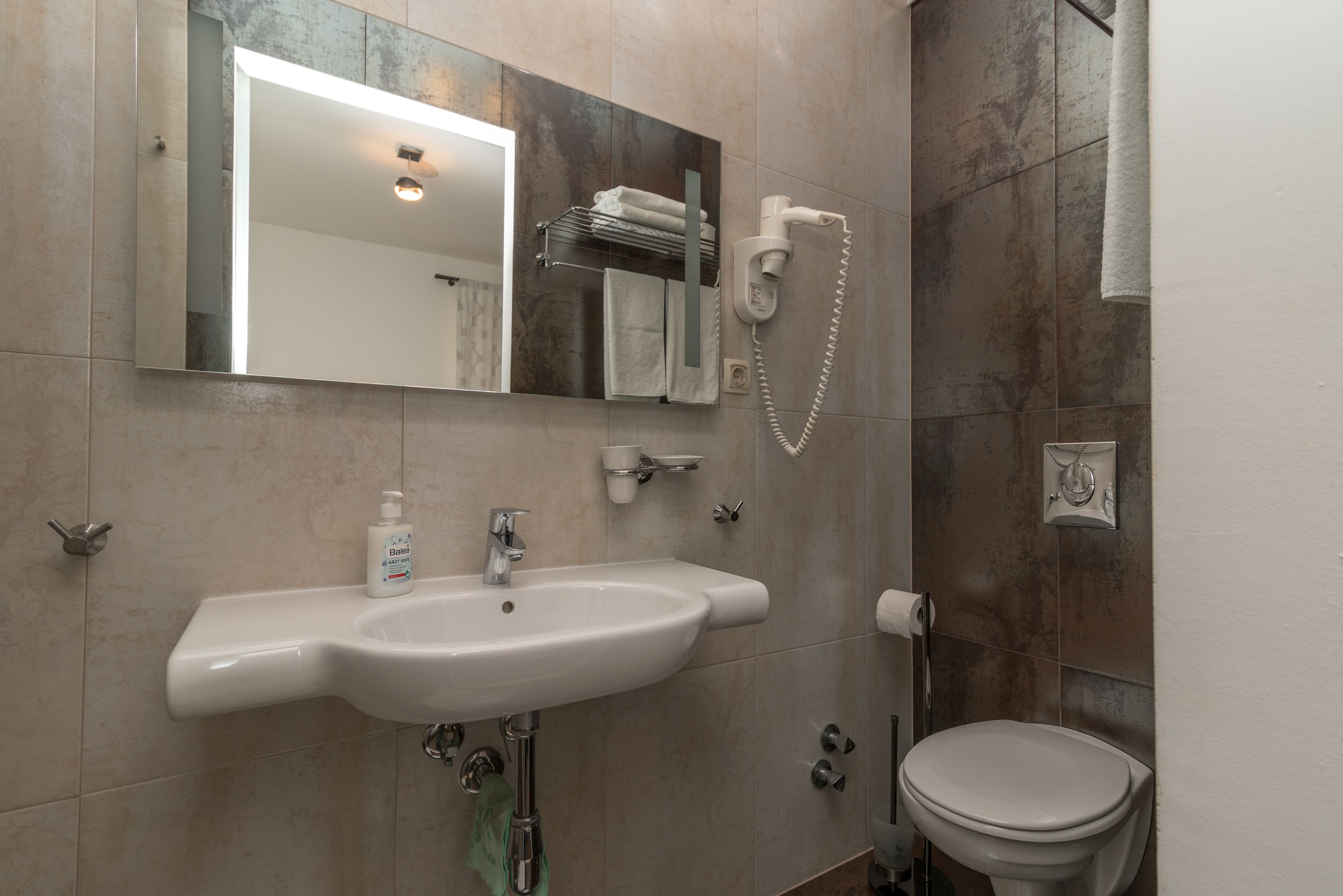 A bathroom with a white sink, a mirror, a towel rack, and a toilet.