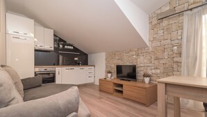 A modern living room with a grey sofa, a wooden TV stand, and a stone wall. - Villa Lucica Trogir (Trogir)