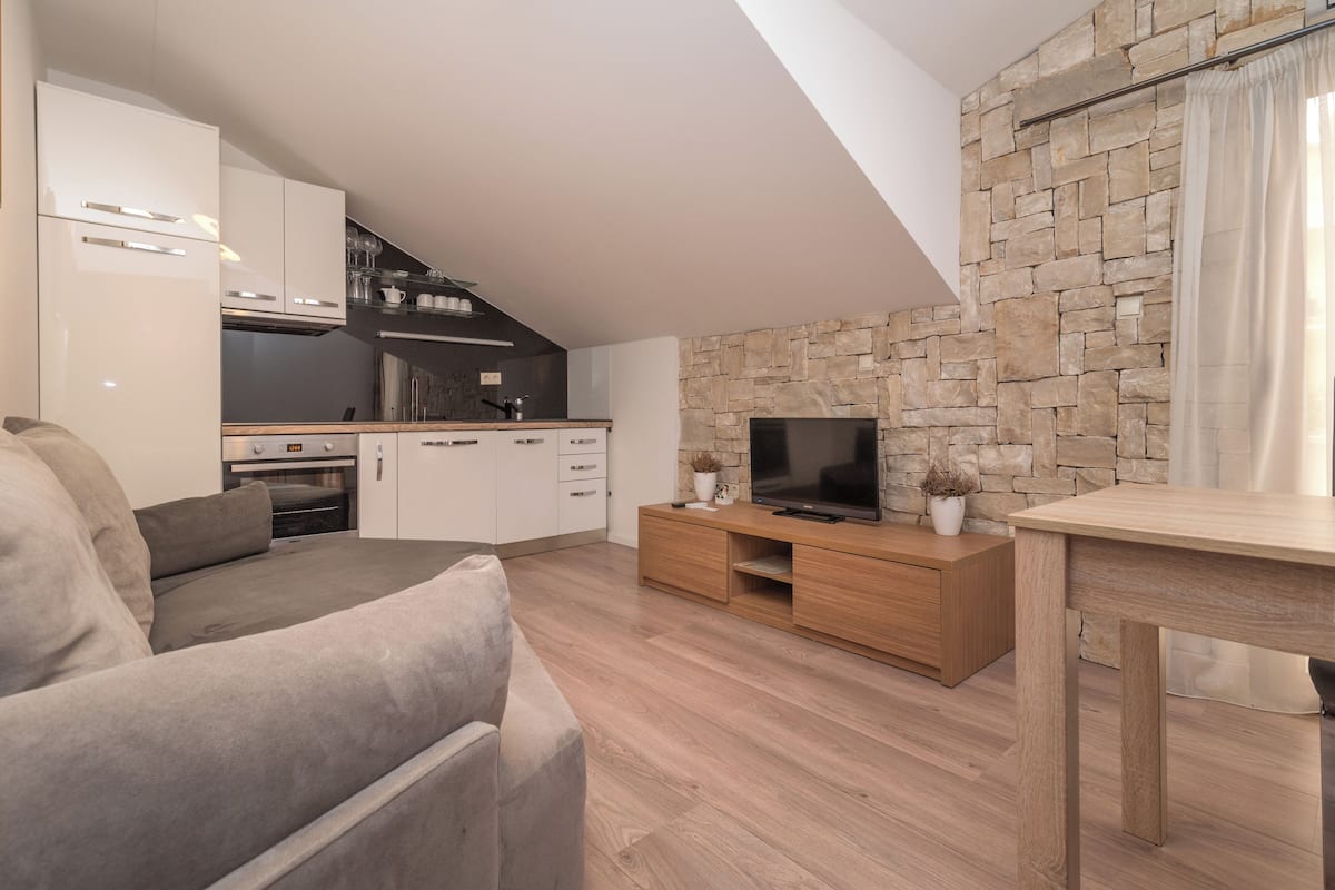 A modern living room with a grey sofa, a wooden TV stand, and a stone wall.
