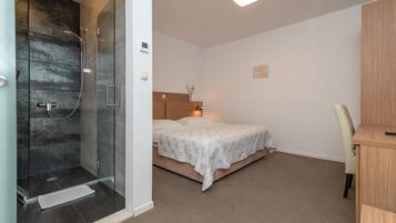 Een slaapkamer met een douchecabine van glas, een bed met hoofdeinde en een bureau met stoel.