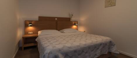 Un dormitorio con cabecera de madera, dos mesitas de noche con lámparas, una colcha estampada y una pequeña obra de arte en la pared.