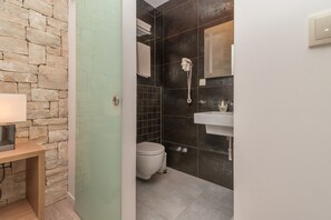 Un baño con pared de piedra, inodoro, lavamanos y ducha con cabezal de ducha manual.
