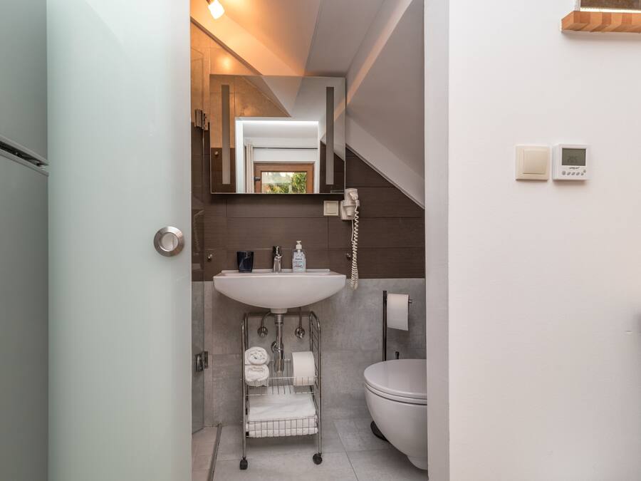 Een moderne badkamer met een wit wastafelmeubel, toilet en een spiegel boven het wastafelmeubel. Er is een handdoekrek met handdoeken en een klein plankje met toiletartikelen.