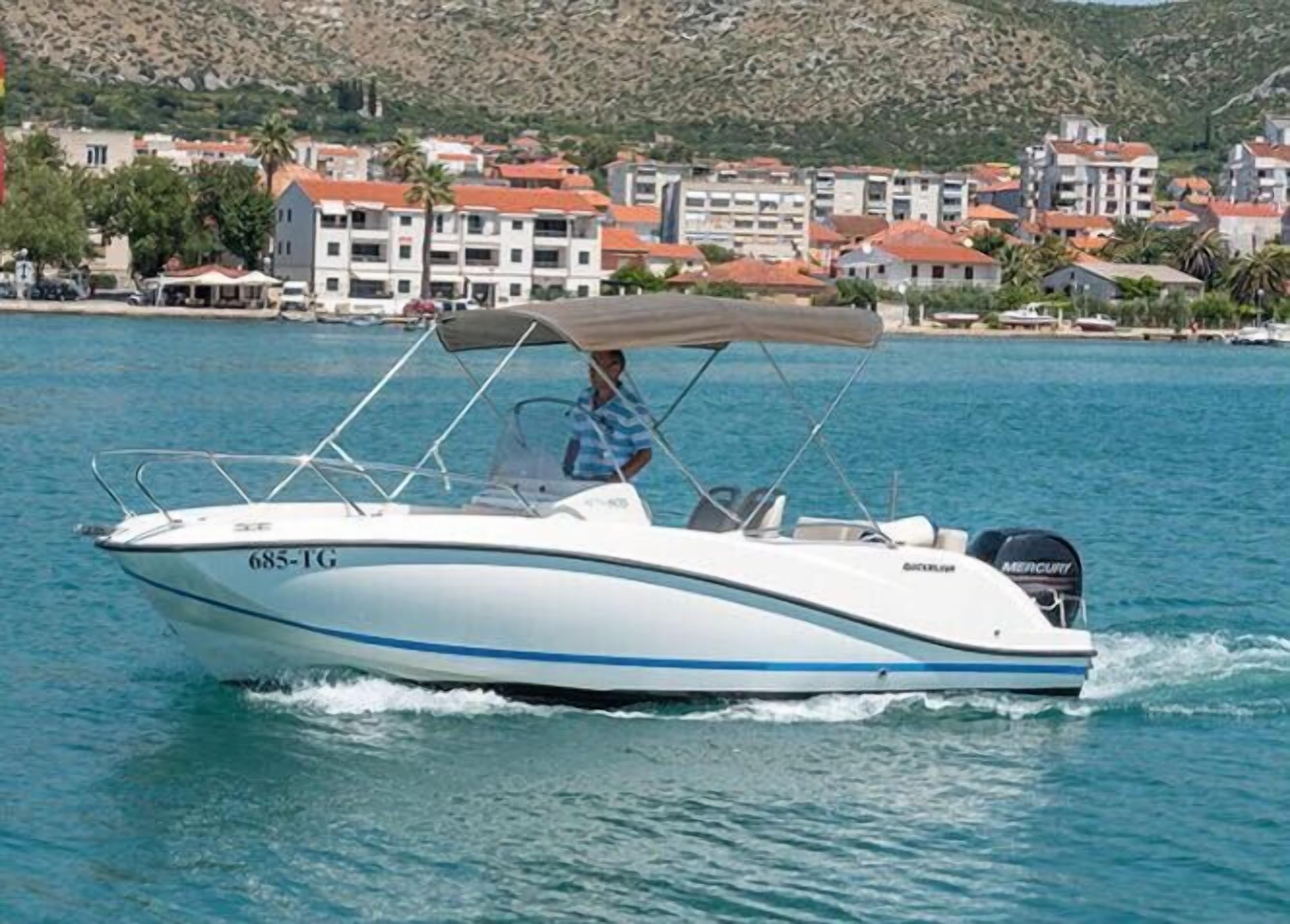 A speedboat with a cabin and a motor, moving on a body of water with a coastal town in the background.